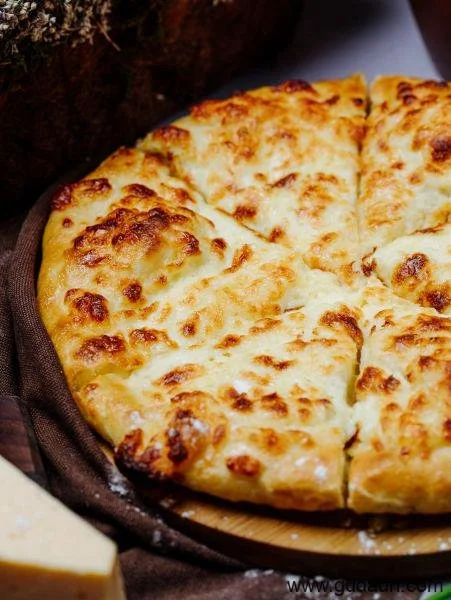 Close-up of a cheesy, baked pizza with a golden crust and melted cheese, sliced and served on a dark plate.