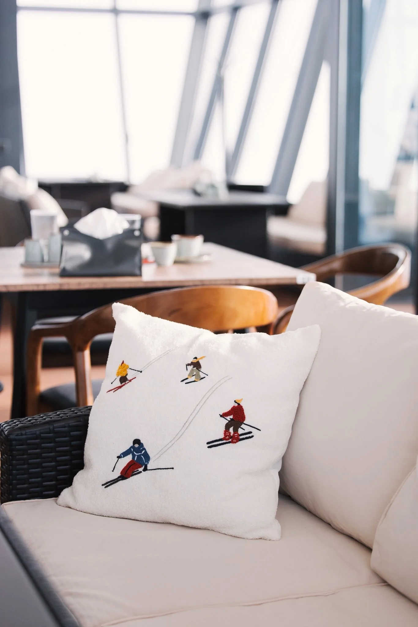 Decorative pillow with embroidered skiers on a sofa in a modern, sunlit room.