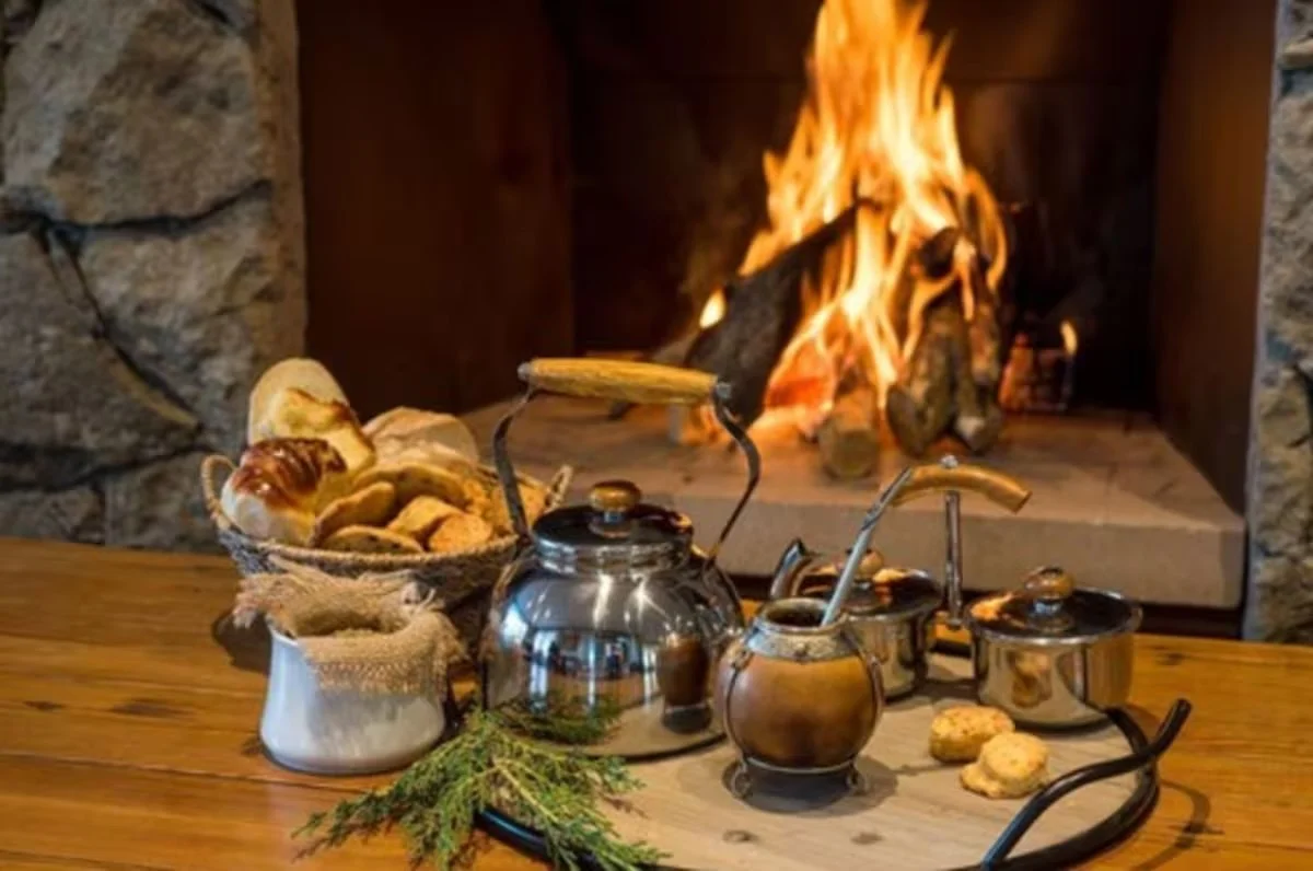 Tea set and baked goods on a wooden table in front of a stone fireplace with a burning fire