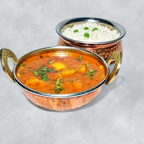 A copper bowl of Indian curry garnished with cilantro, and a copper bowl of white rice topped with green peas, on a light gray surface.