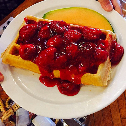 A plate with a waffle topped with cherry pie filling and a slice of cantaloupe melon.