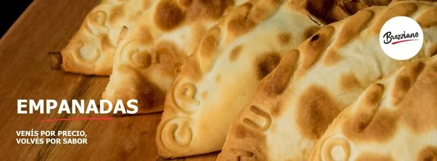 Close-up of several golden-brown empanadas on a wooden surface, with a logo that reads 'Brozziano' in the upper right corner, and the word 'EMPANADAS' in bold white letters on the left along with the phrase 'Venís por precio, volvés por sabor' in sma