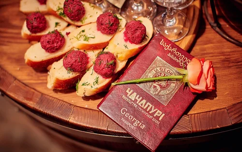 Slices of bread topped with red meat or pâté and garnished with herbs, placed on a wooden platter, with a red hardcover book and a pink rose flower on top.