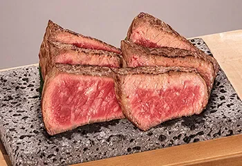 A sliced and seared steak, showing a pink interior, on a black stone slab.