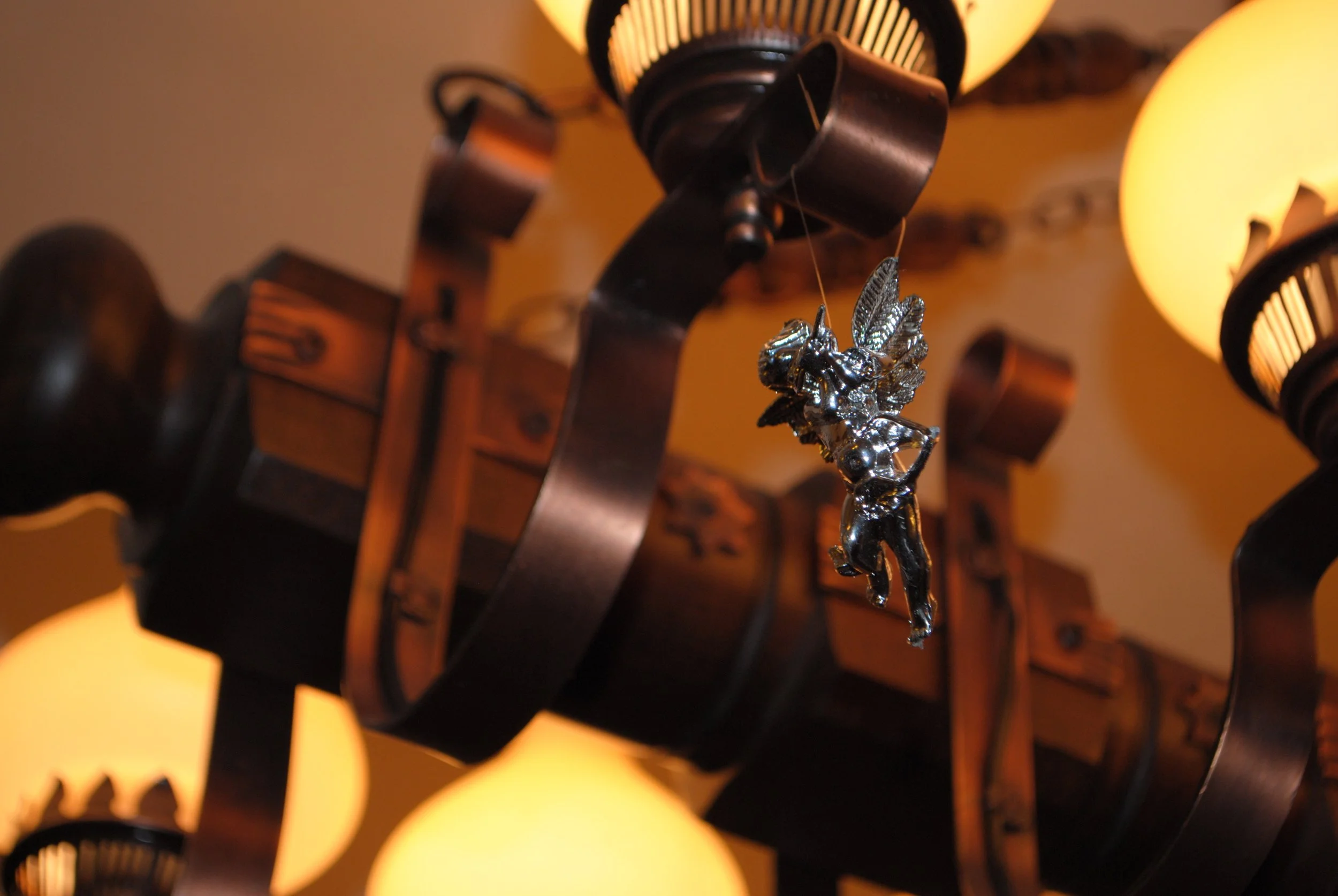 Close-up of a decorative hanging ornament shaped like a fairy standing on a mushroom, with a ceiling light fixture in the background.