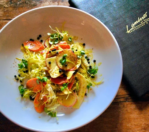 Salad with sliced radishes, carrots, and egg, garnished with microgreens and black pepper on a white plate