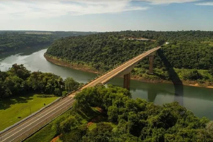 Aerial view of a bridge crossing over a river with green forested hills on both sides.