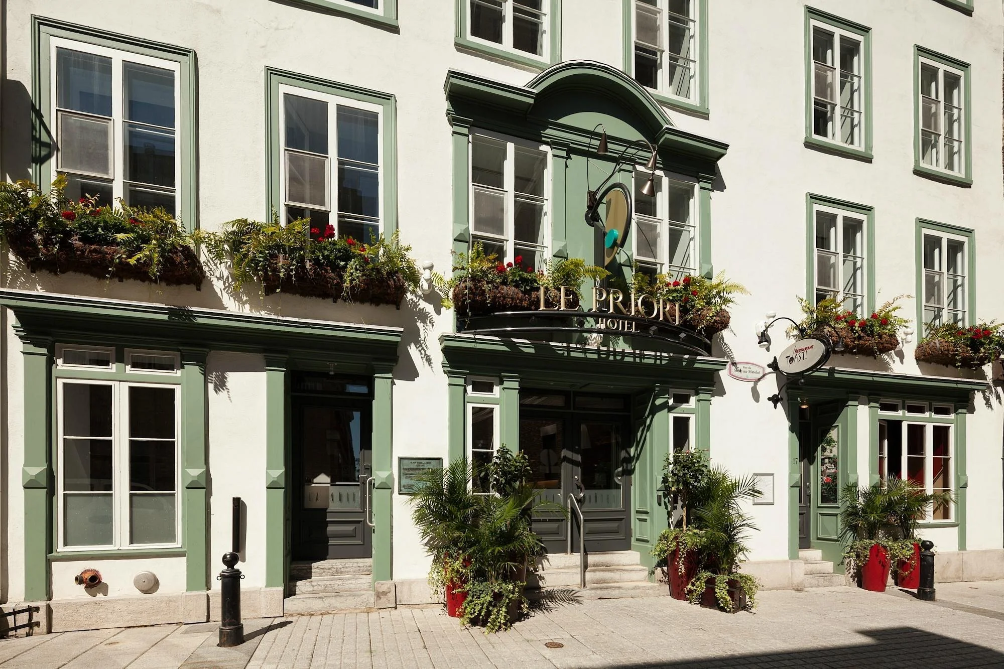 Exterior of Le Priori Hotel with green and white facade, large windows, flower boxes, potted plants, and a sign for the restaurant Osteria.