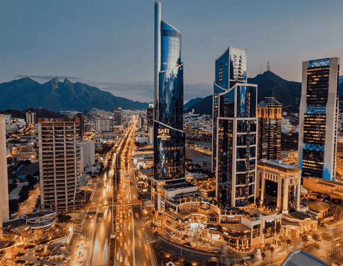 Nighttime cityscape of Dubai with illuminated skyscrapers and mountains in the background.