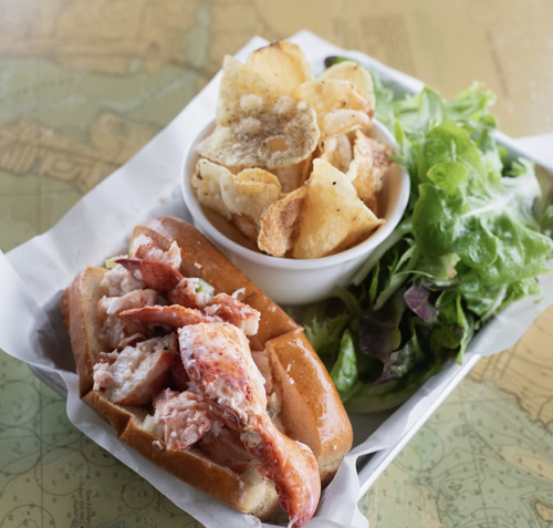 Lobster roll, side of potato chips, and mixed green salad on a tray.