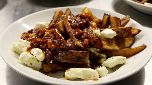 Plate of loaded potato wedges topped with barbecue sauce, cottage cheese, and chopped onions