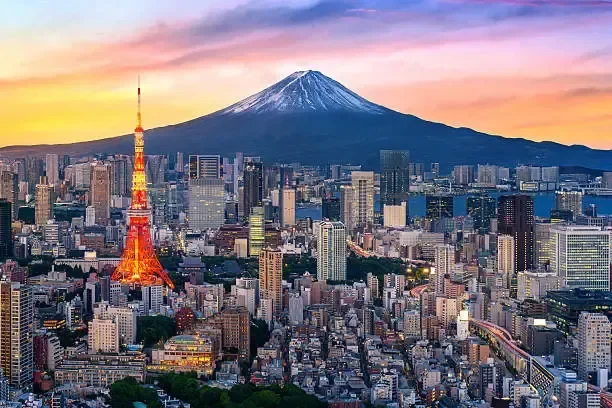 City skyline of Tokyo with Tokyo Tower lit up in orange and Mount Fuji in the background during sunset with a colorful sky.