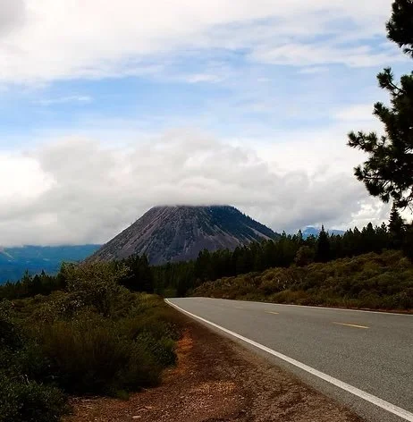 Empty highway leading towards a volcanic mountain with a partly cloudy sky.