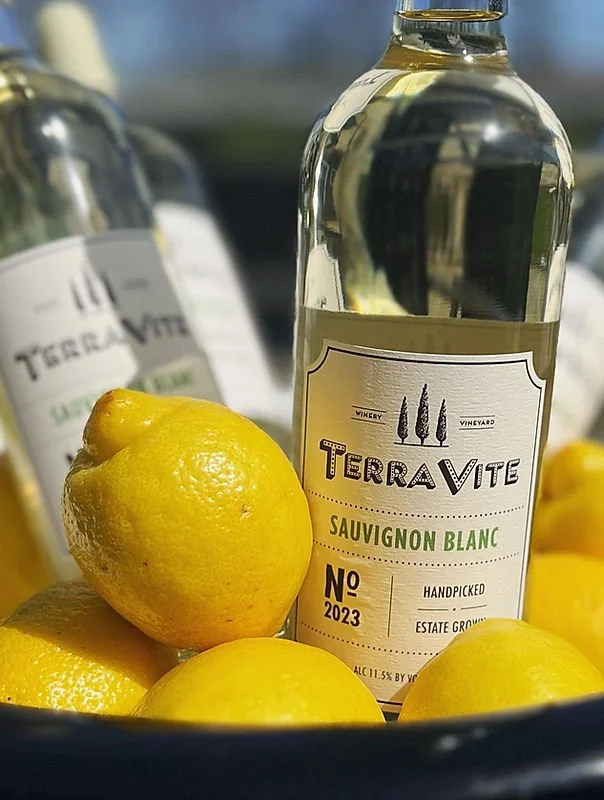 A bottle of TerraVite Sauvignon Blanc wine surrounded by several lemons.