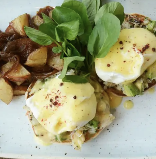 Dish with poached eggs, roasted potatoes, fresh green basil, and other vegetables on a white plate.