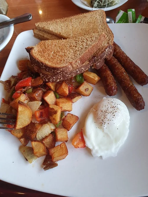 Breakfast plate with fried eggs topped with black pepper, toasted bread slices, cooked breakfast potatoes with diced carrots, onions, and peppers, and three sausage links.