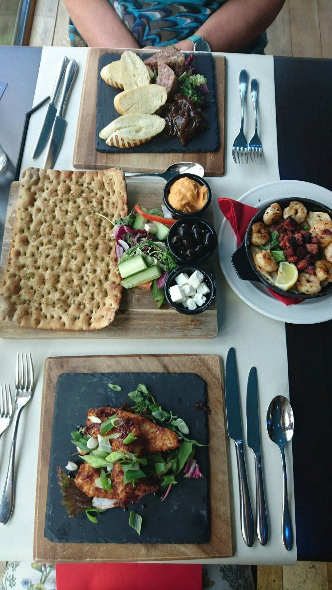 Various dishes on a table, including flatbread, grilled shrimp, salad, and small bowls with sauces and cheese.