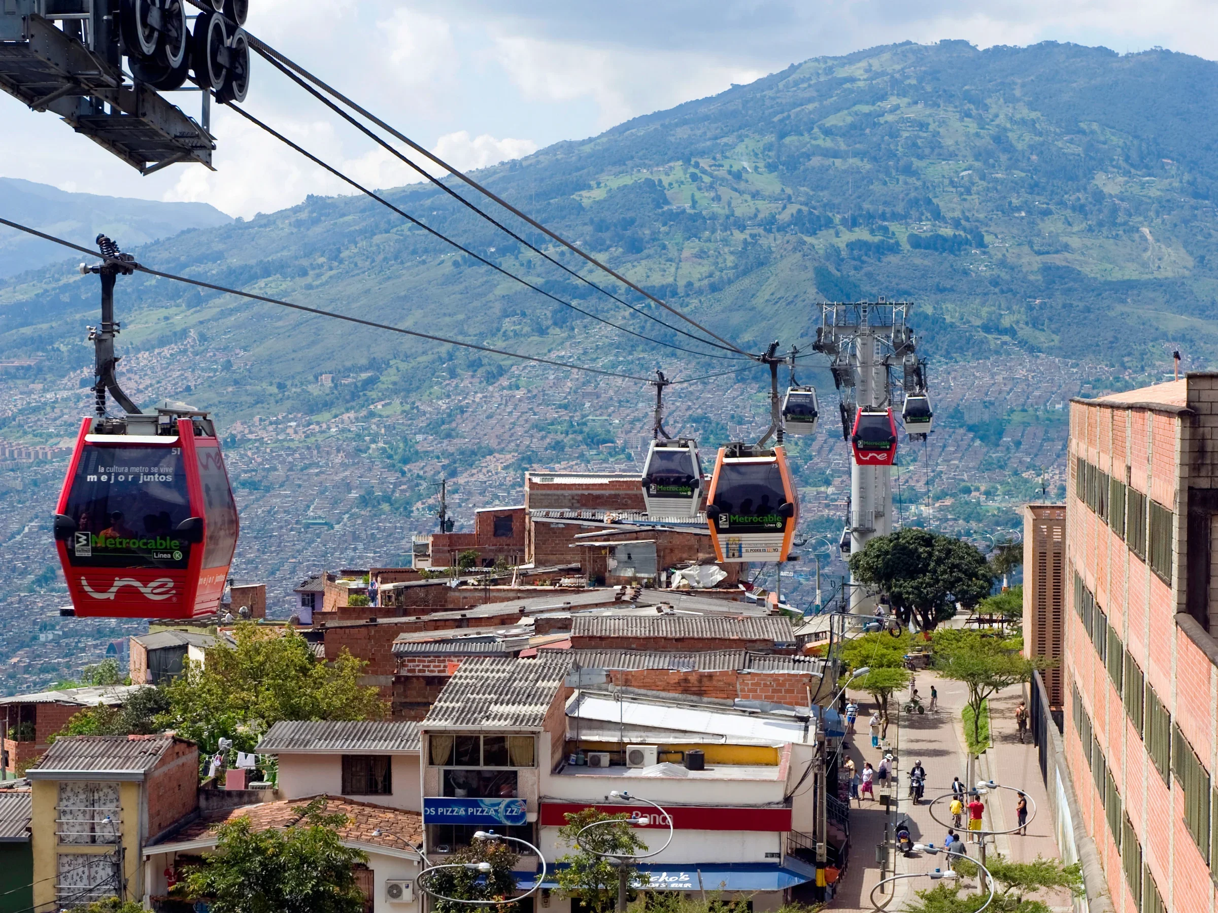 Cable cars moving over a city with residential and commercial buildings, with green mountains in the background.