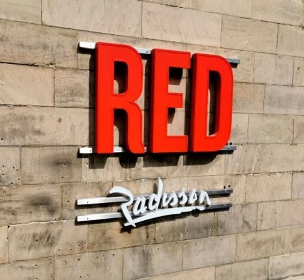 Sign with the word "RED" in large red letters and the word "Radisson" in smaller white script underneath on a brick wall.