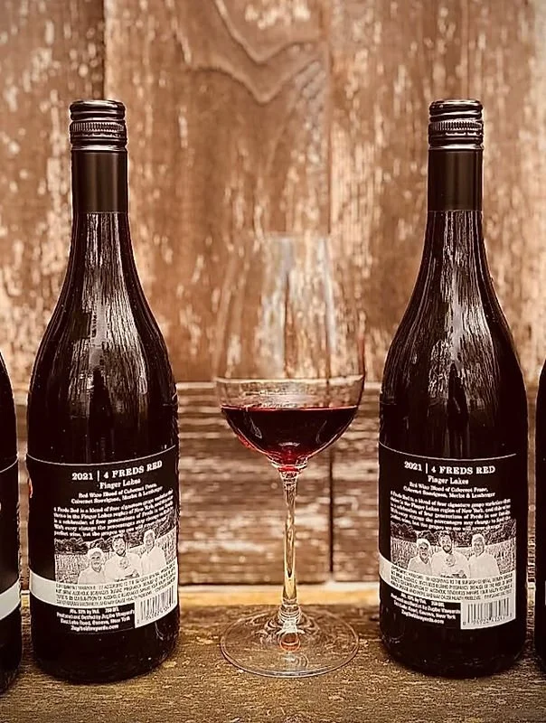 Two bottles of red wine and a glass of red wine in between, set against a wooden background.