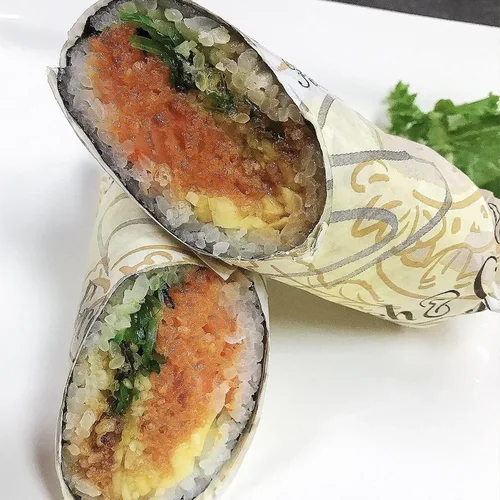Close-up of two cut sushi burritos wrapped in decorative paper, showing rice, vegetables, and seafood filling.