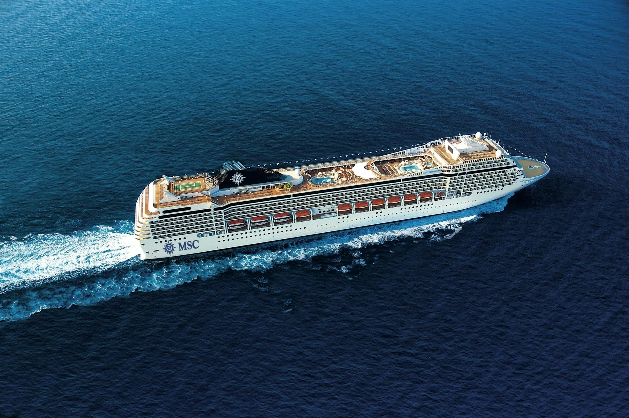 A large cruise ship named Celestyal Discovery docked at a harbor with a smaller ship nearby, surrounded by water and hills in the background.