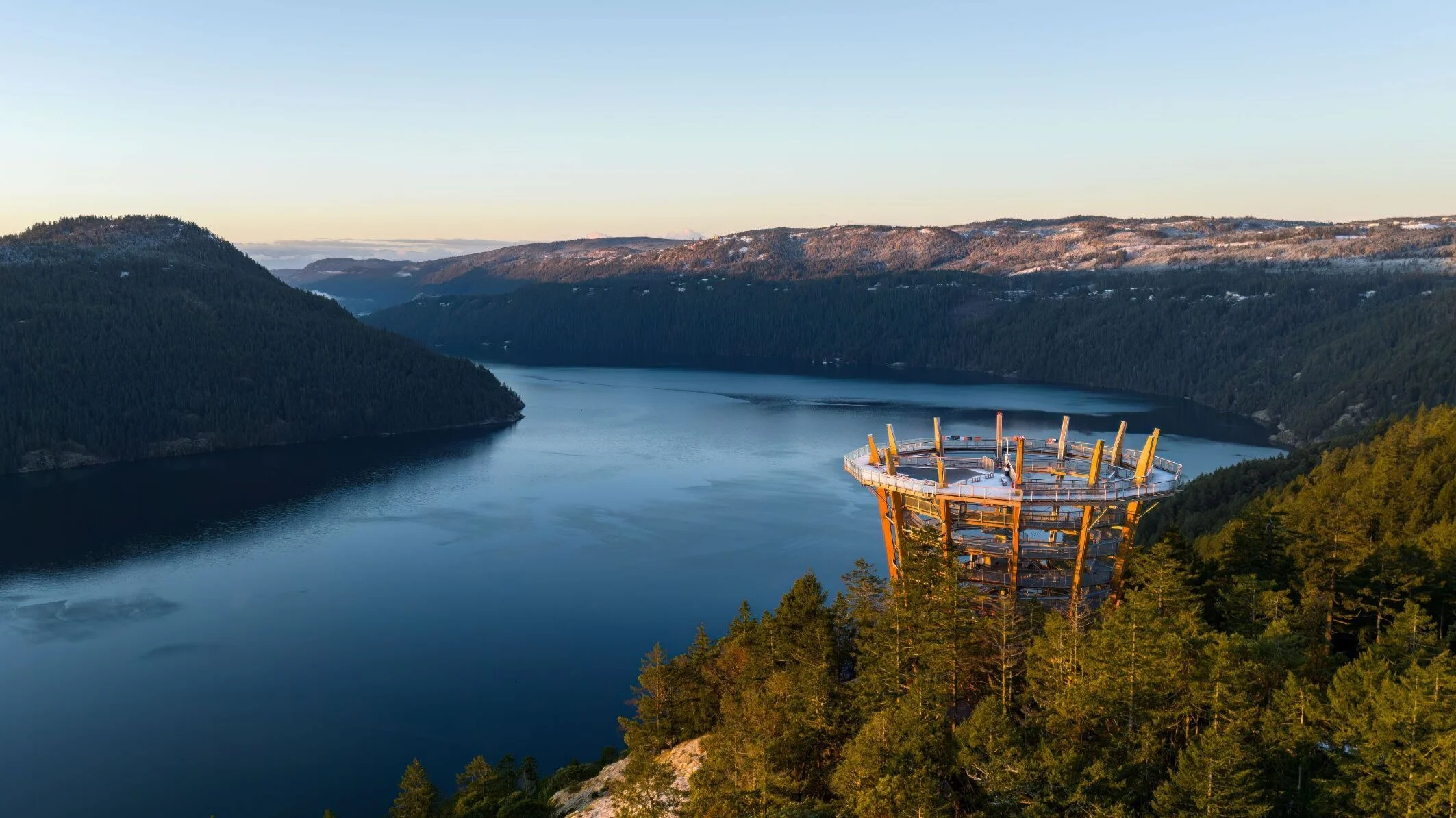 A scenic view of a body of water surrounded by tree-covered hills, with a modern observation tower on the right side of the image.