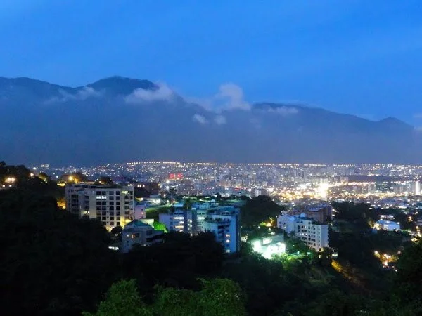 Cityscape at dusk with illuminated buildings and a mountain range in the background.