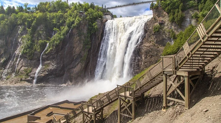 A large waterfall flowing down a rocky cliff with a wooden staircase and walkway built along the side for viewing.