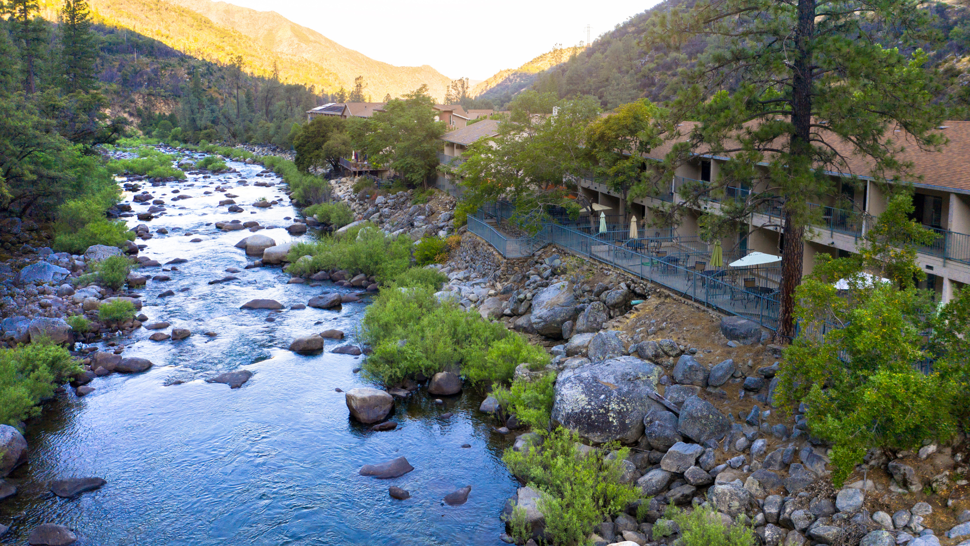 A river flowing through a rocky landscape with trees and mountains, with residential buildings and balconies along the riverbank.