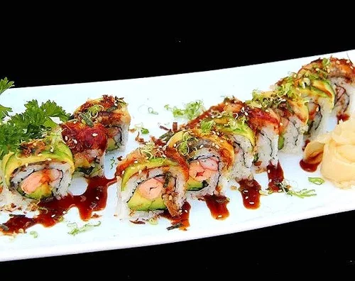 Sushi roll with fish, vegetables, and sauces on a white plate garnished with cilantro and served with pickled ginger and wasabi.