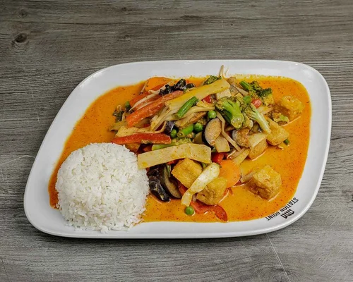 A plate of mixed vegetable curry with white rice on the side, served on a white dish on a wooden table.