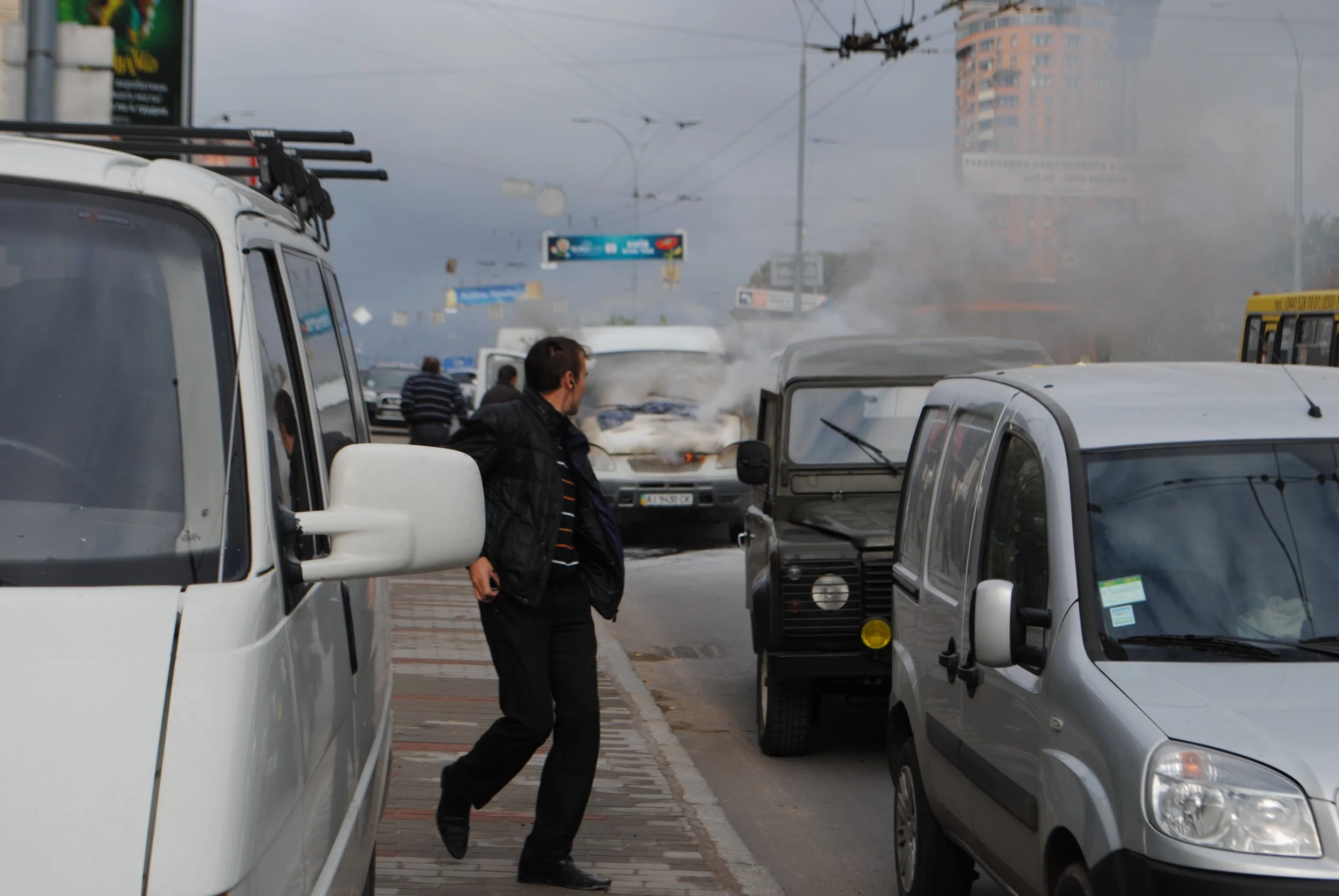 Man walking past parked cars on busy city street with smoke or haze and buildings in the background. Kiev November 2011, Marina Parrish ©