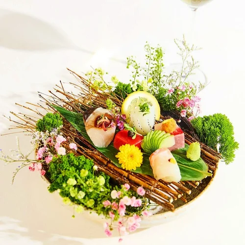 Sashimi on a bed of greenery and flowers arranged on a wooden display.