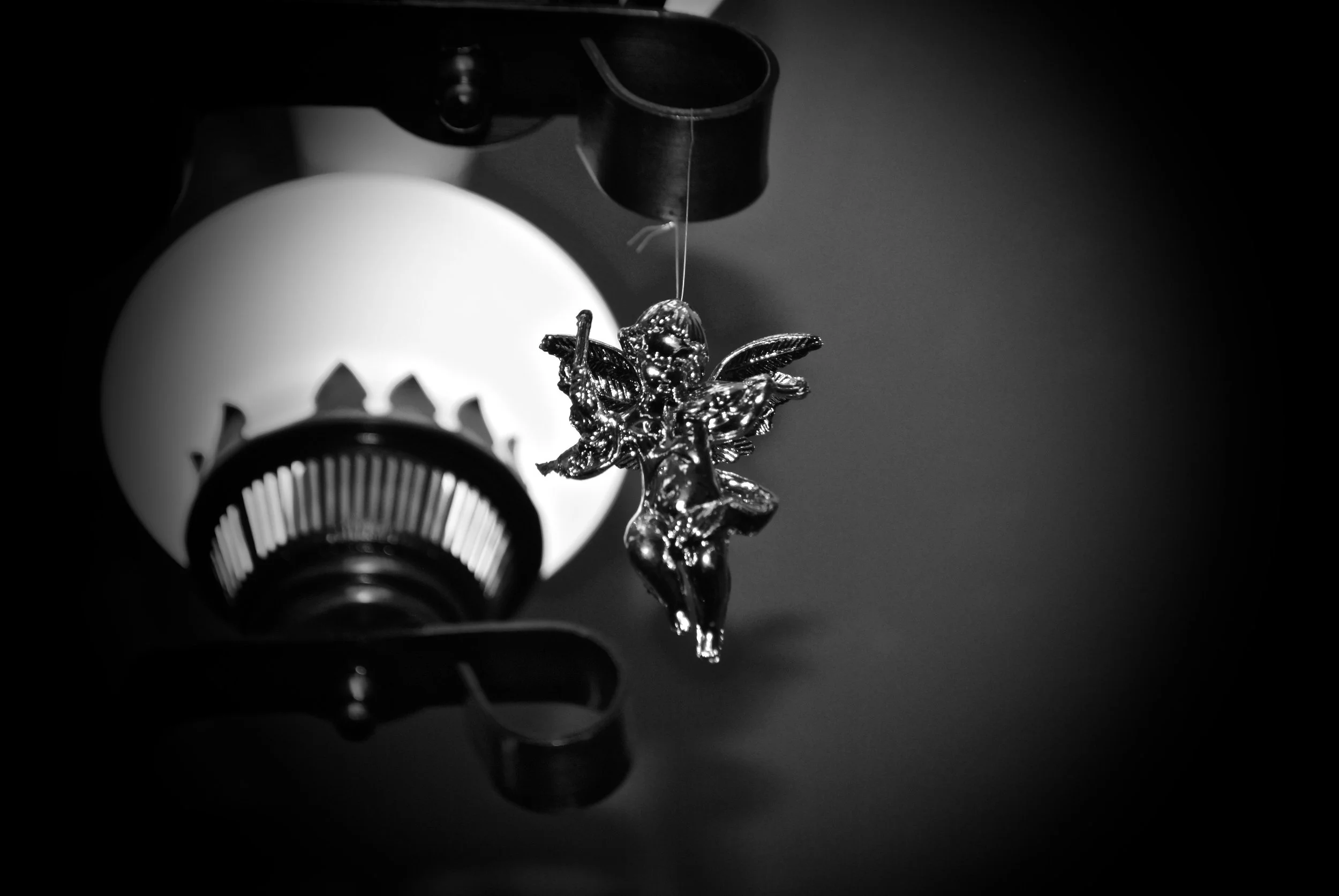 A close-up black and white photo of a decorative angel ornament hanging from a ceiling light fixture.