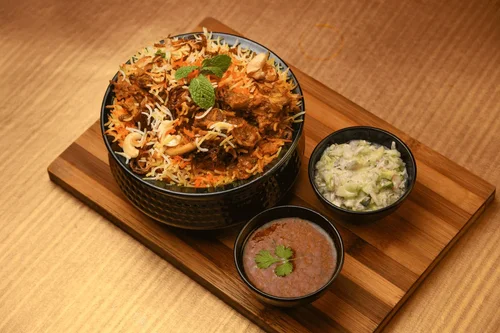 Indian biryani rice with vegetables and meat, served with cucumber raita and tamarind sauce on a wooden tray