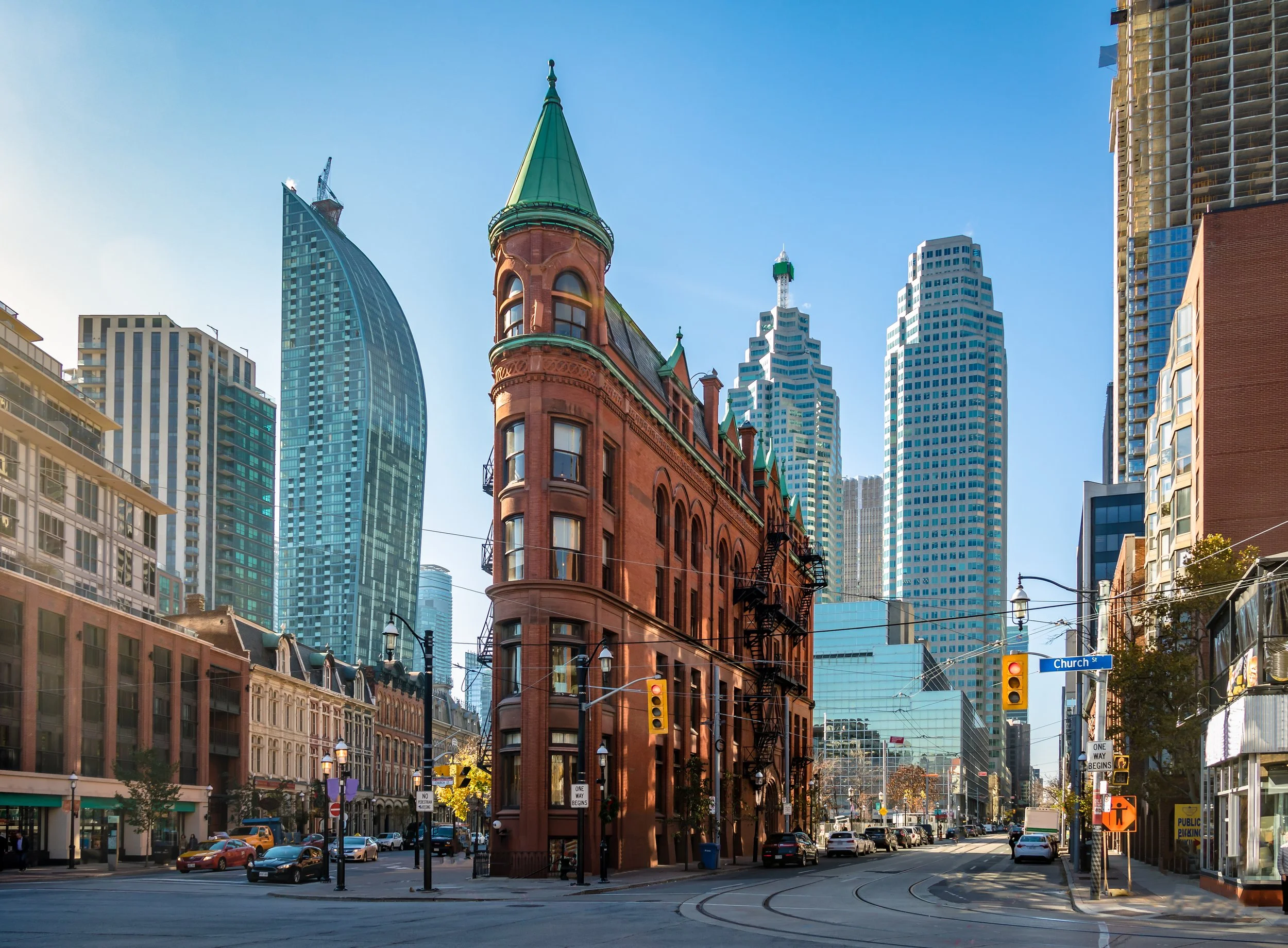 City street scene with historic red brick building on a corner and modern skyscrapers in the background, under a clear blue sky.