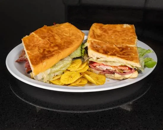 A plate with a sandwich made of toasted bread, lettuce, tomato, and meat, served with potato chips.