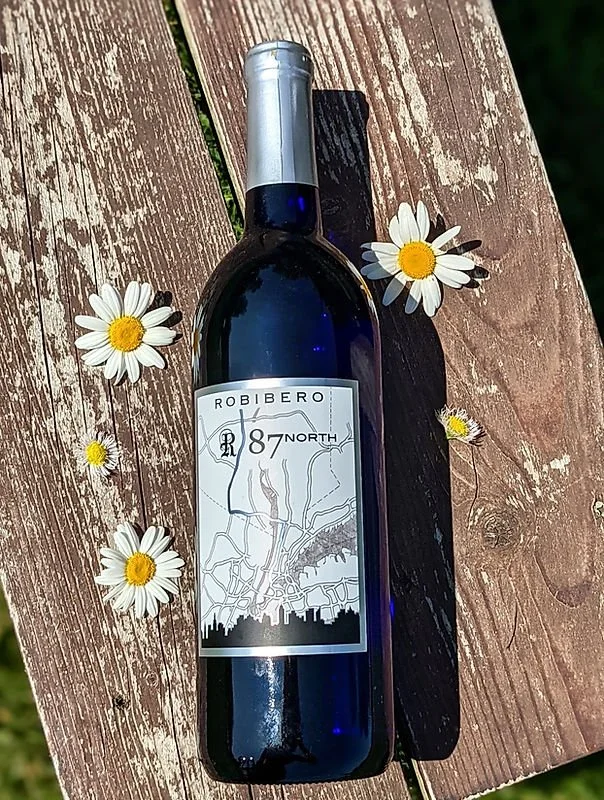 A dark blue wine bottle with a silver cap lying on a wooden surface, surrounded by white daisies with yellow centers.