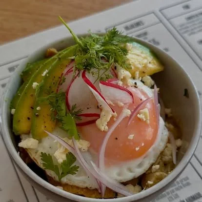 Egg with avocado, radish slices, cilantro, and crumbled cheese in a bowl.