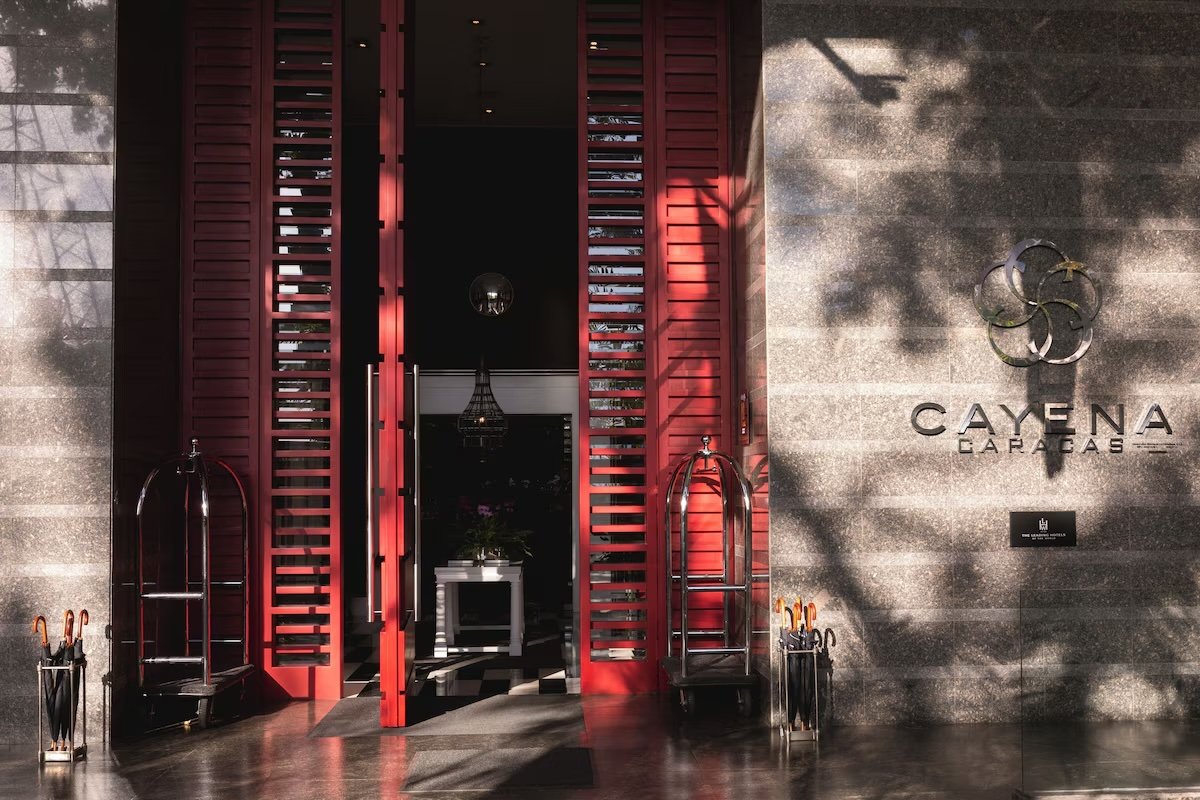 Entrance to Cayena Carib Beach hotel with red shutter doors, luggage carts, and a logo on the wall.