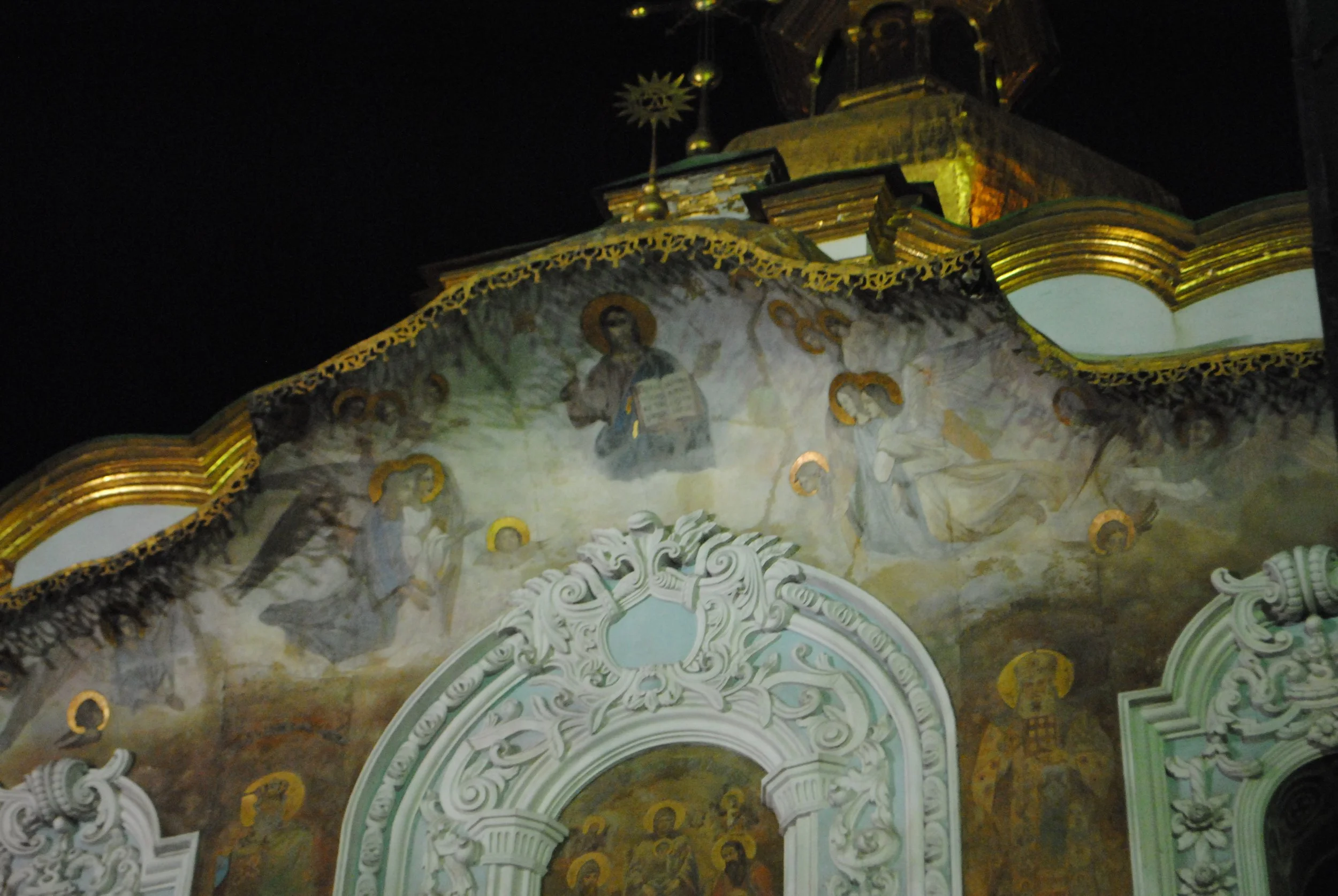 Close-up of ornate church facade at night with detailed religious artwork, angels, and gold accents.