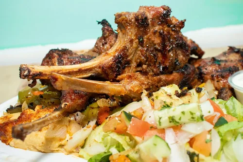 Grilled meat with vegetables and salad on a white plate.