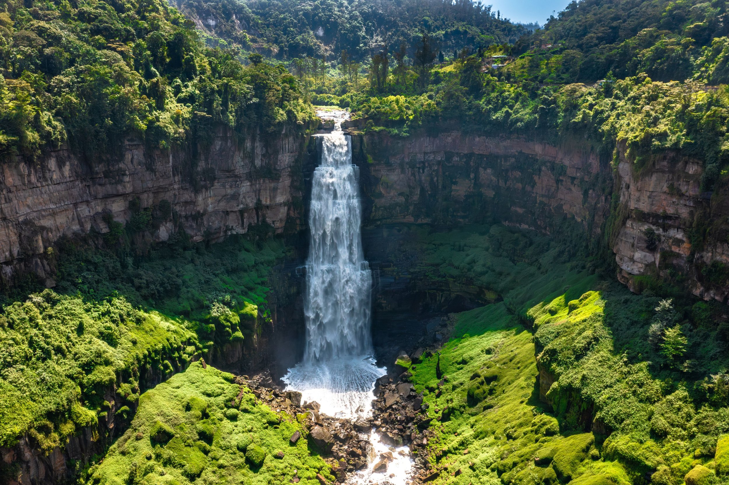 A tall waterfall flowing down a steep cliff surrounded by lush green forest and vegetation.