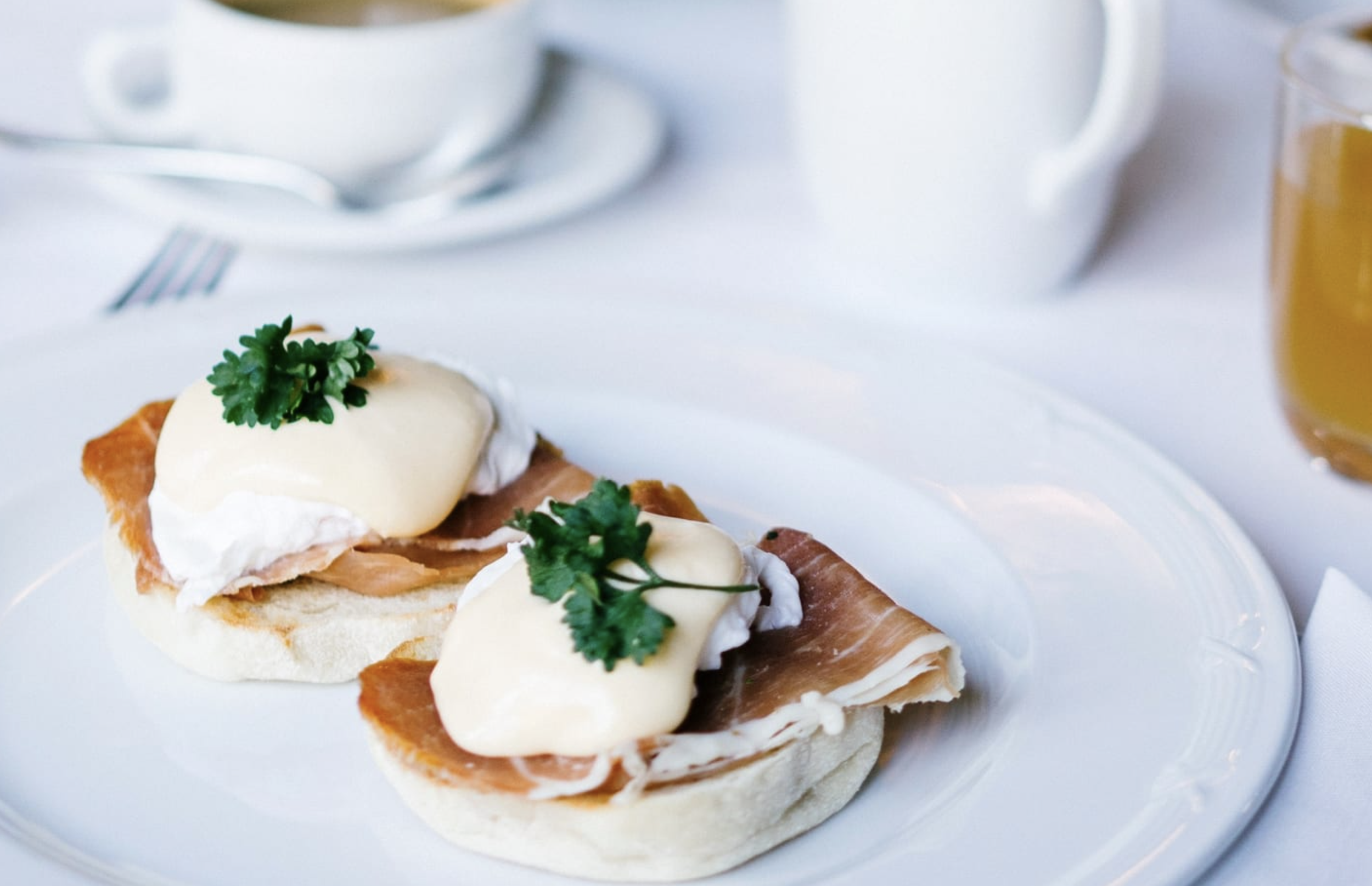 Two pieces of bread topped with poached eggs, slices of ham, and garnished with parsley on a white plate.