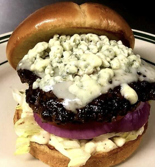 A burger with blue cheese crumbles, purple onion slices, lettuce, and sauce in a toasted bun.