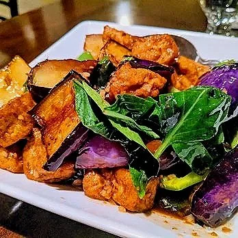 Plate of fried tofu topped with eggplant and fresh green leafy herbs.