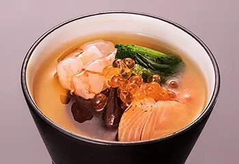 A bowl of seafood soup with salmon, shrimp, vegetables, and fish roe