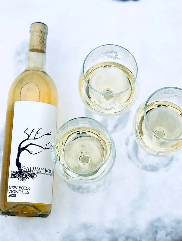 A bottle of white wine next to three glasses filled with white wine on a white surface.