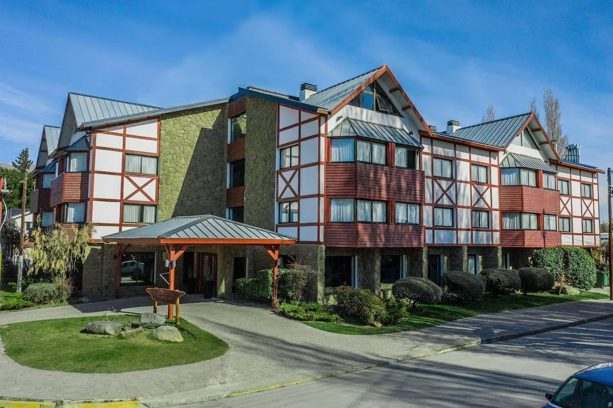 Multi-story residential building with red and white exterior, green accents, metal roof, landscaped lawn, and a covered entrance.